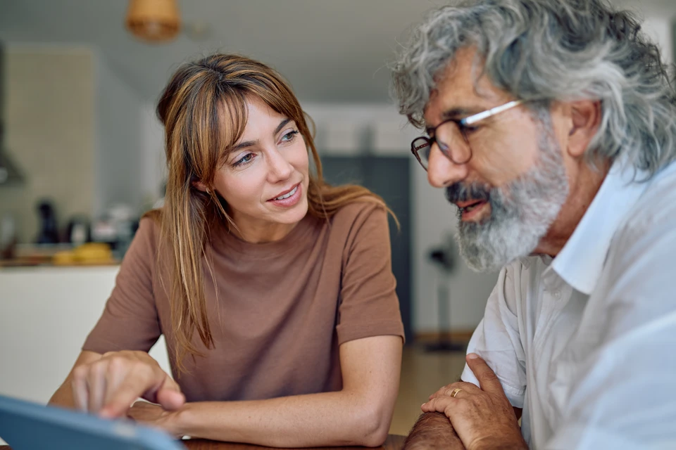 Gros plan professionnel d'une main de conseiller présentant un document ou un formulaire d'aide financière (MaPrimeRénov', CEE ou éco-PTZ) à un client en train de le consulter, dans un cadre intérieur modern de type bureau ou salon, avec éventuellement des plans ou devis de rénovation énergétique visibles en arrière-plan. La scène doit transmettre la confiance et la clarté administrative d'une démarche de subvention accompagnée par un professionnel expert.