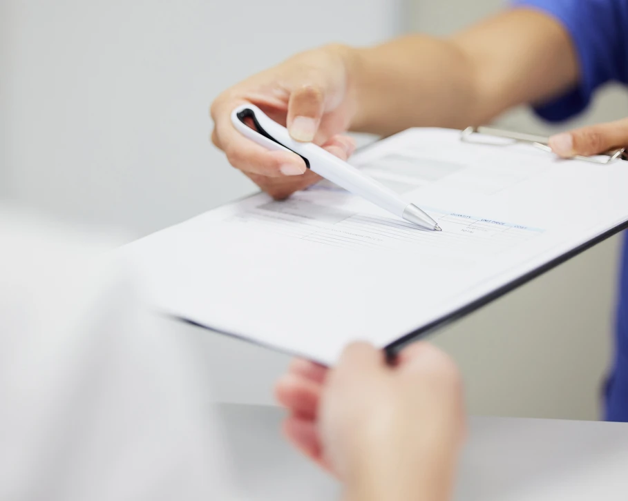 Main droite tenant un stylo à bille blanc, écrivant sur carnet à spirale ouvert posé sur bureau en bois clair